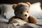 A sick teddy bear with a bandage on his head lies in bed with a fever and a headache.