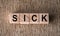 SICK word written on wooden blocks on a brown background