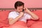 Sick young cauacsian man coughing while lying in bed and speaking on phone with doctor