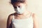 Sickly-looking girl in protective medical mask looks sadly at the camera