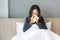 Sickness Asian woman sneezing into a tissue in bed room after wake up. Female illness from colds or flu. Allergy or health problem