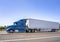 Side of blue big rig semi truck tractor transporting frozen cargo in refrigerator semi trailer driving on the wide multiline