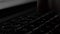 Side Close up male hand typing in dark room with laptop backlit keyboard.