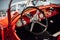 A side, close up view of red restored retro cabriolet interior: black steering wheel, dashboard with speedometer