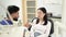 Side closeup view of attractive male dentist checking and selecting color of young asian woman teeth