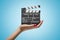 Side closeup of woman`s hand facing up and holding clapperboard on light-blue gradient background.