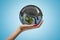 Side closeup of woman`s hand facing up and holding small Earth covered in black oli-like liquid on light blue background