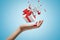 Side closeup of woman`s hand facing up and levitating white gift box that has started to break into small pieces on