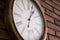 Side closeâ€“up of a wooden wall clock with roman numerals hanging in a red brick wall.