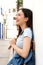 Side laughing young woman standing with backpack on street