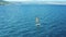 Side panning aerial shot of person practicing a windsurfing on waves, in the sea in summer.