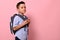 Side portrait of a schoolboy with a school bag on his back on pink background with copy space. Back to school concepts