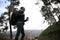 Side portrait of a young man with backpack and travel mug, during a trekking in the forest, mountains on the background