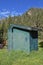 Side profile of a an old green outhouse in a mountainous and wooded area.