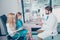 Side profile photo of male brunet bearded doc,examining a a small cute blond girl patient in ophthalmology laboratory, she sits w