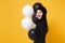 Side profile view Arabian muslim woman in hijab celebrating hold black white air balloons isolated on yellow background