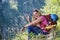 Side profile of woman mountaineer with helmet attached to backpack, sitting in grass with her hand raised as a victory sign.