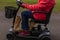 A side on shot of an elderly lady in a red coat enjoying the freedom of an electric mobility scooter.