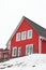 A side shot of a red wooden house with several white windows with a dark roof. Clear white sky is on top of the frame. White snow