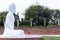 Side shot of a white colored Buddha statue in meditative pose with green trees and concrete strunctures behind