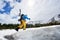 Side of snowboarder hidden face with snowboard on his back on snowy slope. Clouds on blue sky on background. Low angle