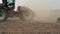 A side view of an agricultural tractor, plowing a field, soil dust. close-up