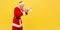 Side view of angry screaming elderly man with gray beard wearing santa claus costume holding megaphone and yelling with aggressive