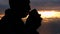 Side view of Asian senior drinking hot coffee outdoor and enjoying the beautiful sky landscape at sunset on the mountain top.