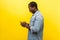 Side view of astonished man using cellphone, typing text message or dialing number. isolated on yellow background