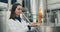 Side view of attractive female worker holding and looking at freshly made beer in glass tube. Process engineer in lab