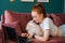 Side view of attractive young woman lying on comfortable sofa with white pretty spitz pet dog and using laptop.