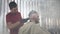 Side view of barber in black gloves and red t-shirt. The hairdresser shaves the nape of the client. A lot of smoke