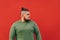 Side view of a bearded hispanic guy with a stylish haircut, frowning, looking seriously aside, standing in front of the red wall