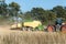 Side view of big modern tractor machine with baler trailer making hay blocks after wheat field harvesting. Agricultural