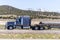 Side view of big rig American dark blue semi truck transporting covered cargo on flat bed semi trailer going on divided highway