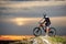 Side view of biker on mountain bike at top of rock restingwit blurred background of the sunset sky