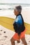 Side view of biracial senior woman in wetsuit walking with yellow surfboard at sunny beach