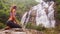 Side view blond girl sits in yoga pose in front of waterfall