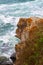 Side view of the brown part of the rock in the shape of a monkey against the background of a rough blue sea with large waves