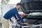 Side view of brunette man standing near open car hood.