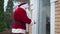 Side view burglar in red costume with white beard looking around breaking in house. Caucasian man in Santa Clause outfit