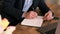 Side view of businessman in suit filling out planner or notepad next to an open laptop against of fresh bouquet of