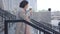 Side view, camera following brunette adult woman running down the stairs with coffee cup and folder with documents and