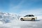 Side view of a car standing by a huge snowdrift formed after cleaning roads. The concept of cleaning roads from snow