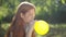 Side view carefree teenage redhead girl blowing yellow balloon sitting in sunrays in spring summer park. Portrait of