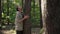 Side view Caucasian man standing at tree trunk looking up in woodland. Male traveler enjoying calm spring summer day in