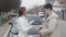 Side view of Caucasian mature senior woman giving car keys to young brunette girl in front of new black automobile