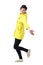 Side view of cheerful young woman in yellow raincoat running with spread arms looking at camera