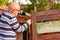 Side view close up photo portrait of senior man hammering nail into wooden fency.