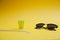 Side view of colorful straws, glass and sunglasses on yellow background, with copy space